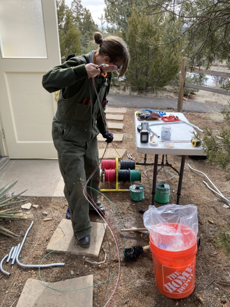 NPS worker pulls electrical wire outside near table with tools.